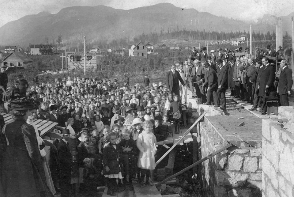 A black and white photograph of a crowd gathering around a stone foundation.